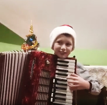 Chłopiec w czapce Mikołaja gra na akordeonie