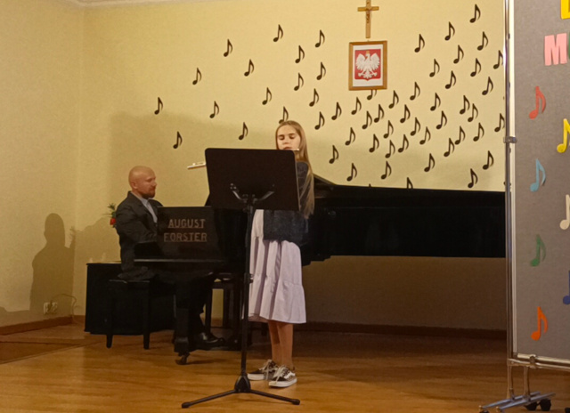 Dziewczynka gra na flecie poprzecznym, nauczyciel akompaniuje na fortepianie